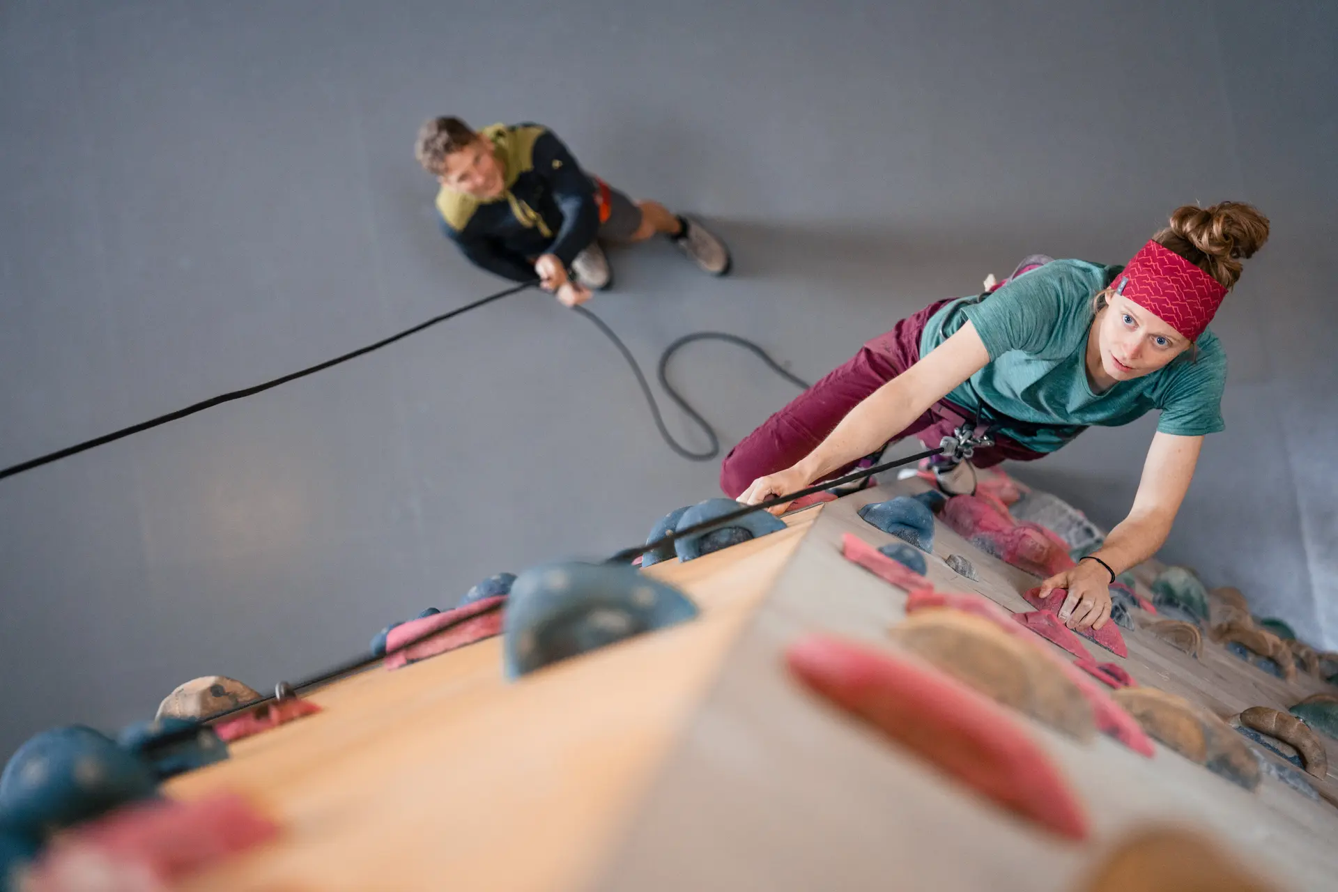 Eine Frau klettert in einer Kletterhalle, ihr Partner sichert sie. | © DAV / Julian Rohn